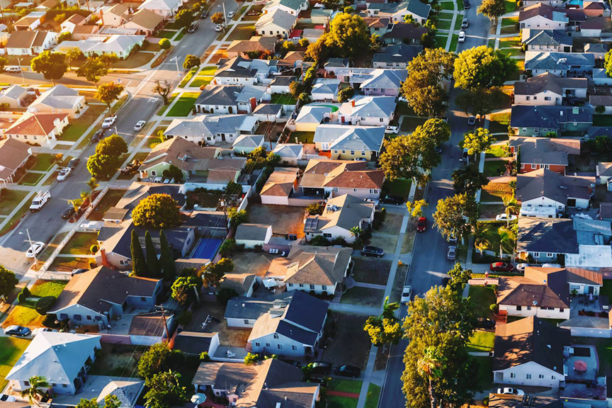 Residential neighborhood aerial featuring green lawns and trees at sunset.