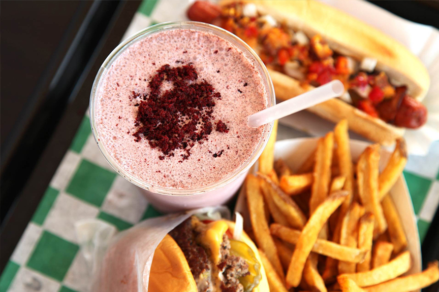 A bird’s eye view of a trayed Harlem Shake meal featuring a strawberry shake, burger, hotdog and fries.