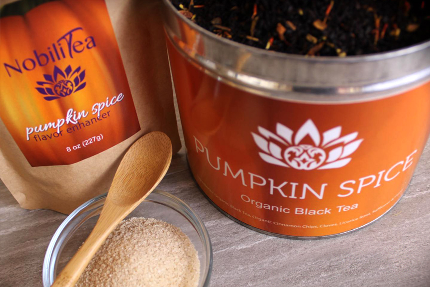 Focus on an open jar of Pumpkin Spice NobiliTea and a bag of Pumpkin Spice flavor enhancer. Orange labels featuring the NobiliTea logo.