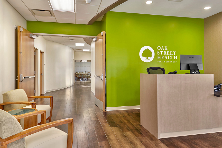 Brightly lit reception area featuring Oak Street Health’s signature lime green accent wall and logo.