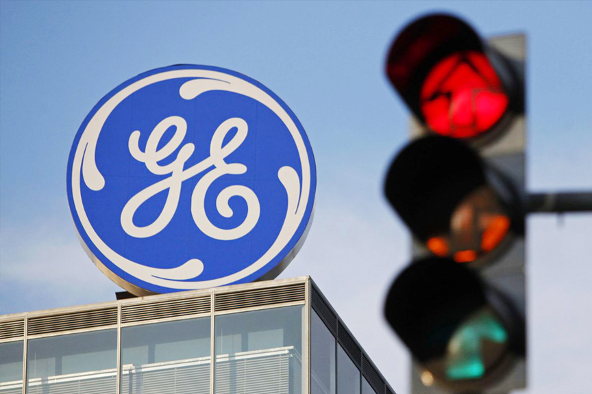 Focus on a blue GE sign and building exterior. An out of focus stop light in the foreground.