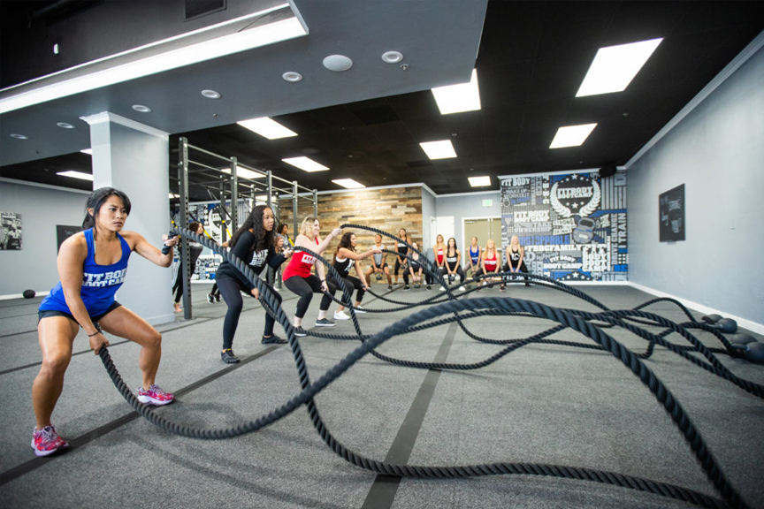Fit Body Boot Camp interior. Female clients engaging in a battle rope workout.