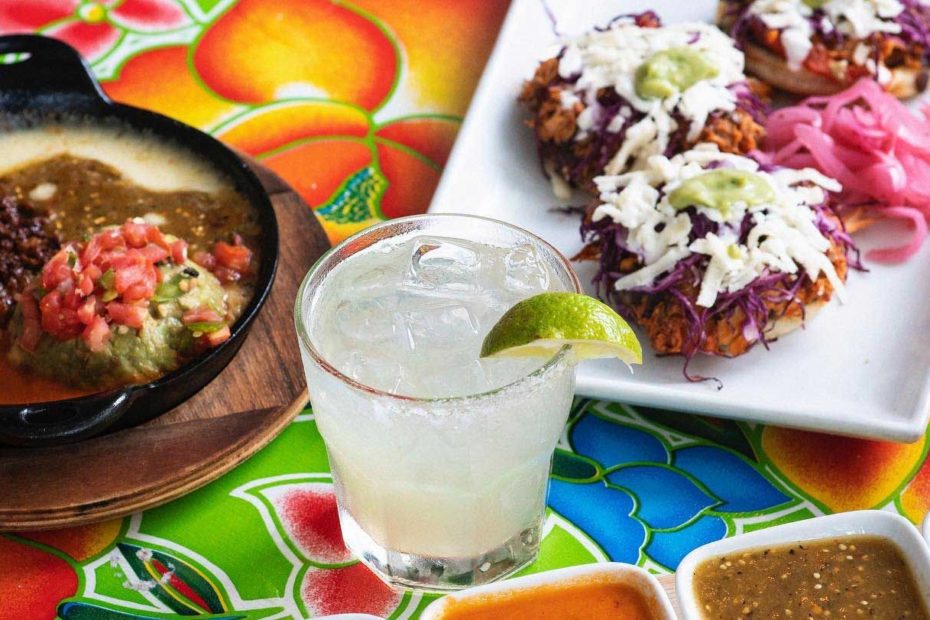 A margarita glass with a lime wedge sitting on a table surrounded by plates of tex-mex.