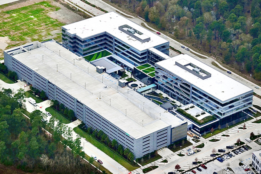 Aerial view of Hewlett Packard Headquarters, flanked by a forested area, adjacent to a parking lot, in Houston, TX on a sunny day.