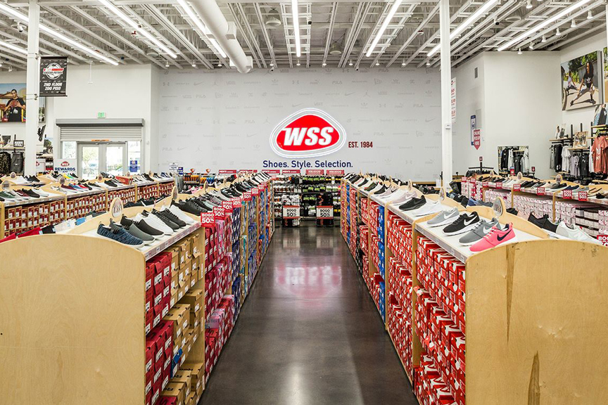 WSS retail store interior featuring rows of tennis shoes, red boxes, and the red WSS company logo on the back wall.